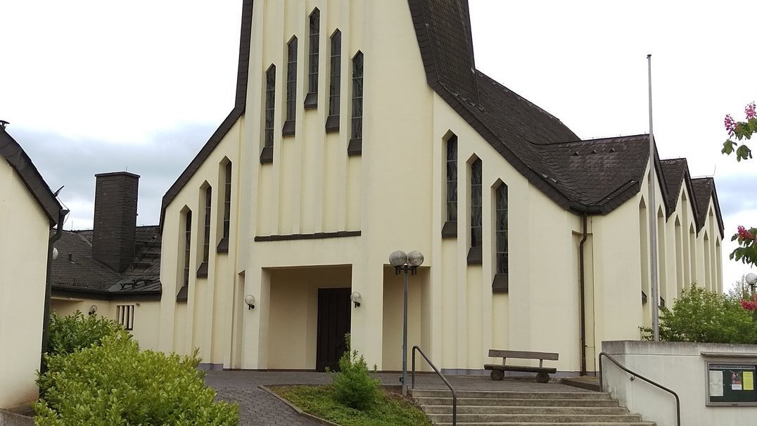 moderne Kirche mit sehr langem spitzen Kirchturm und länglichen Fenstern