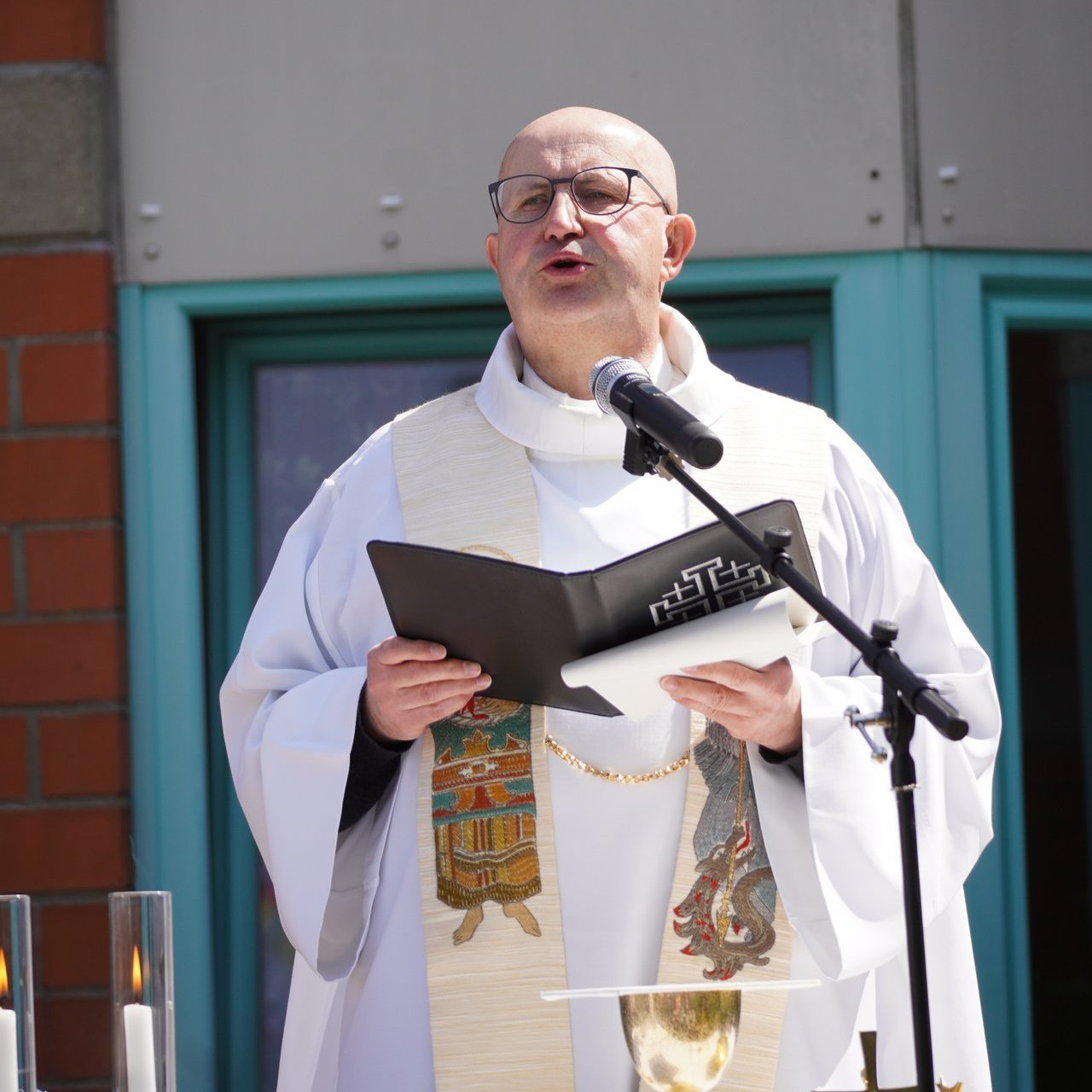Ein Pater des Deutschen Ordens im Messgewand steht am Mikrofon und liest aus einer schwarzen Mappe.