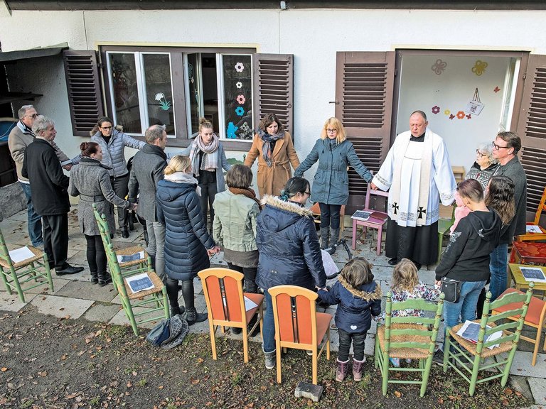 Stuhlkreis auf der Terasse: ein Pater spricht scheinbar ein Gebet - alle stehen und halten sich an den Händen